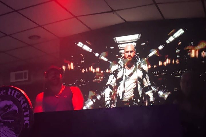 The DJ at the booth in front of the video wall, with the Heretic's eagle logo sign at left