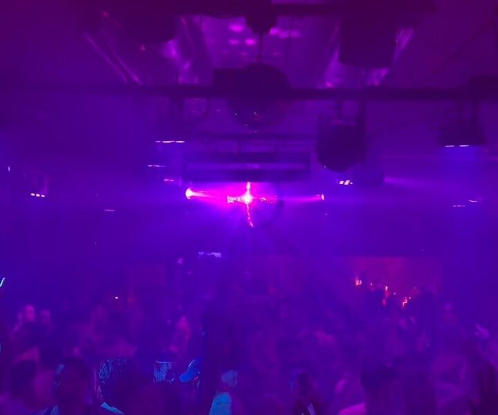 A crowd on the dance floor under purple light and a mirror ball at the Heretic